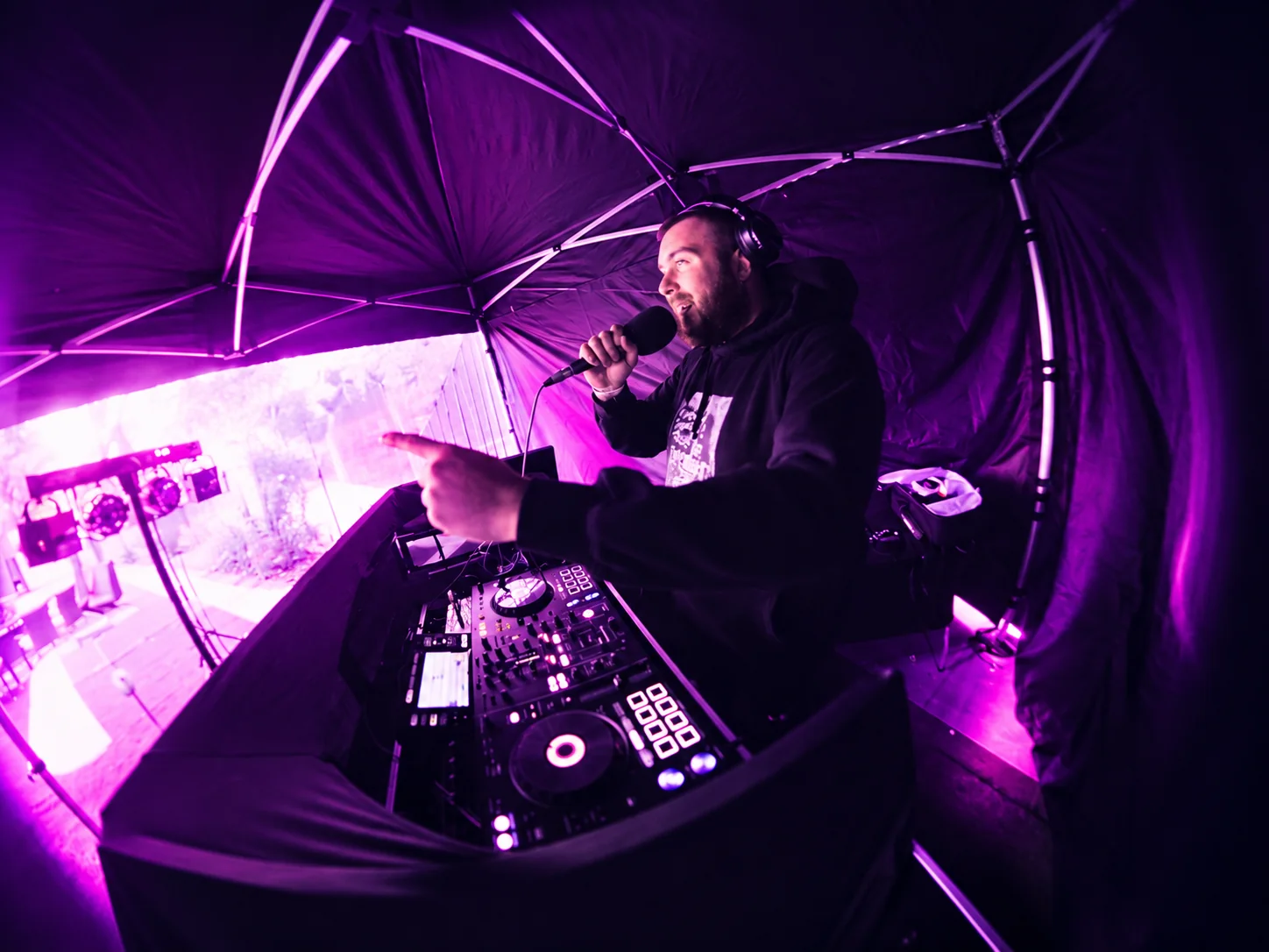 Paulyy Pudd performing with a microphone behind the DJ decks